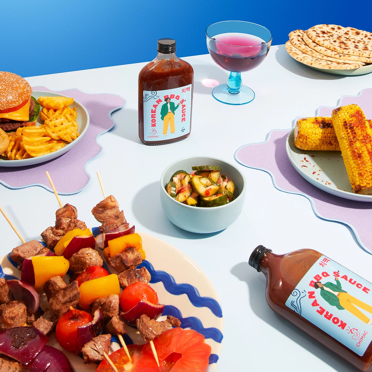 Table with food including skewers, sauces, and drinks against a blue background