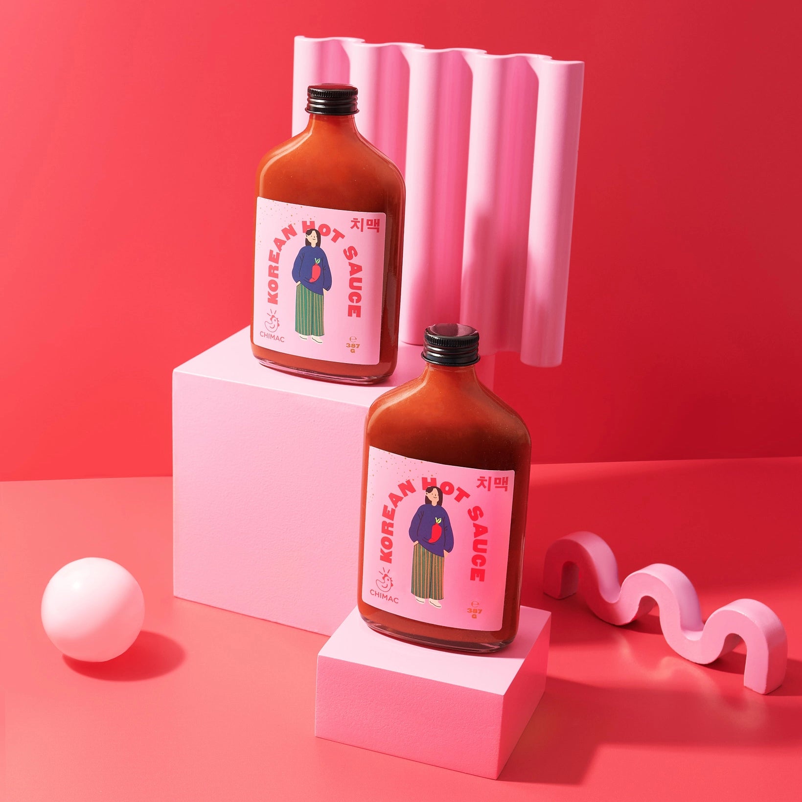 Two bottles of Korean hot sauce on pink platforms with a pink background